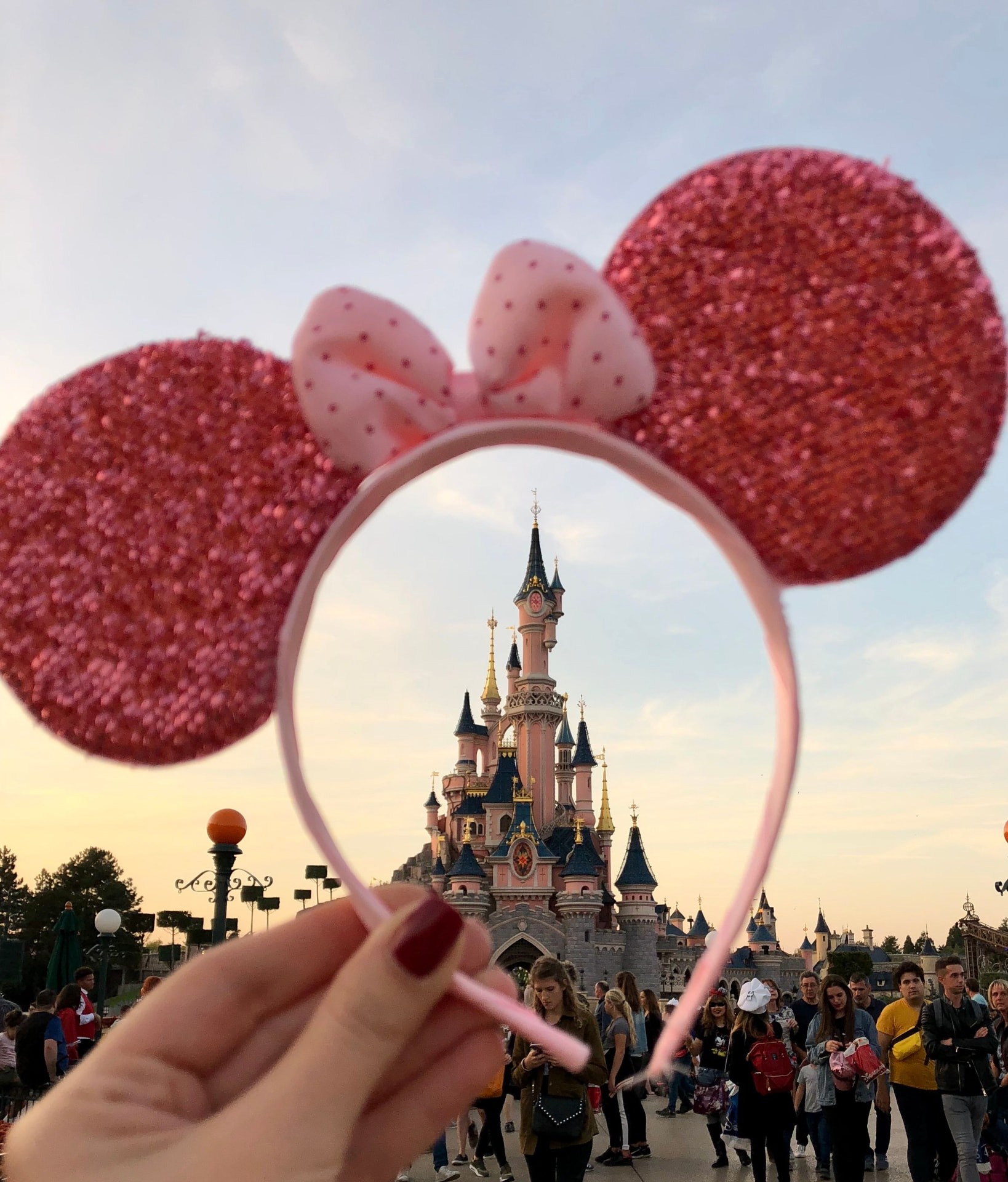 Sparkling pink ear headband held up in a park