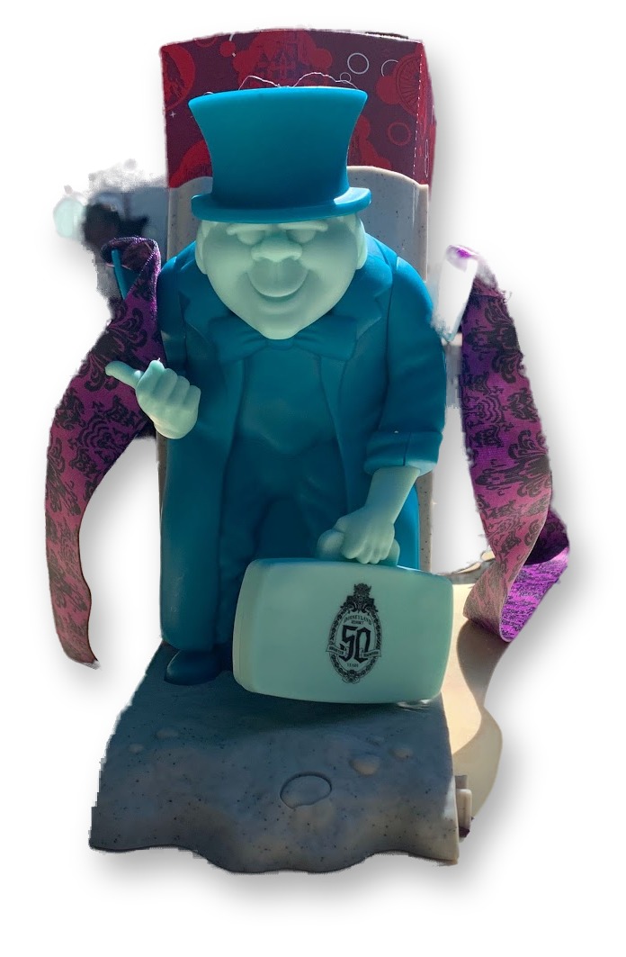 Light-up Phineas Plump tombstone-shaped popcorn bucket with purple Haunted Mansion wallpaper strap, photographed on an outdoor table at Disneyland