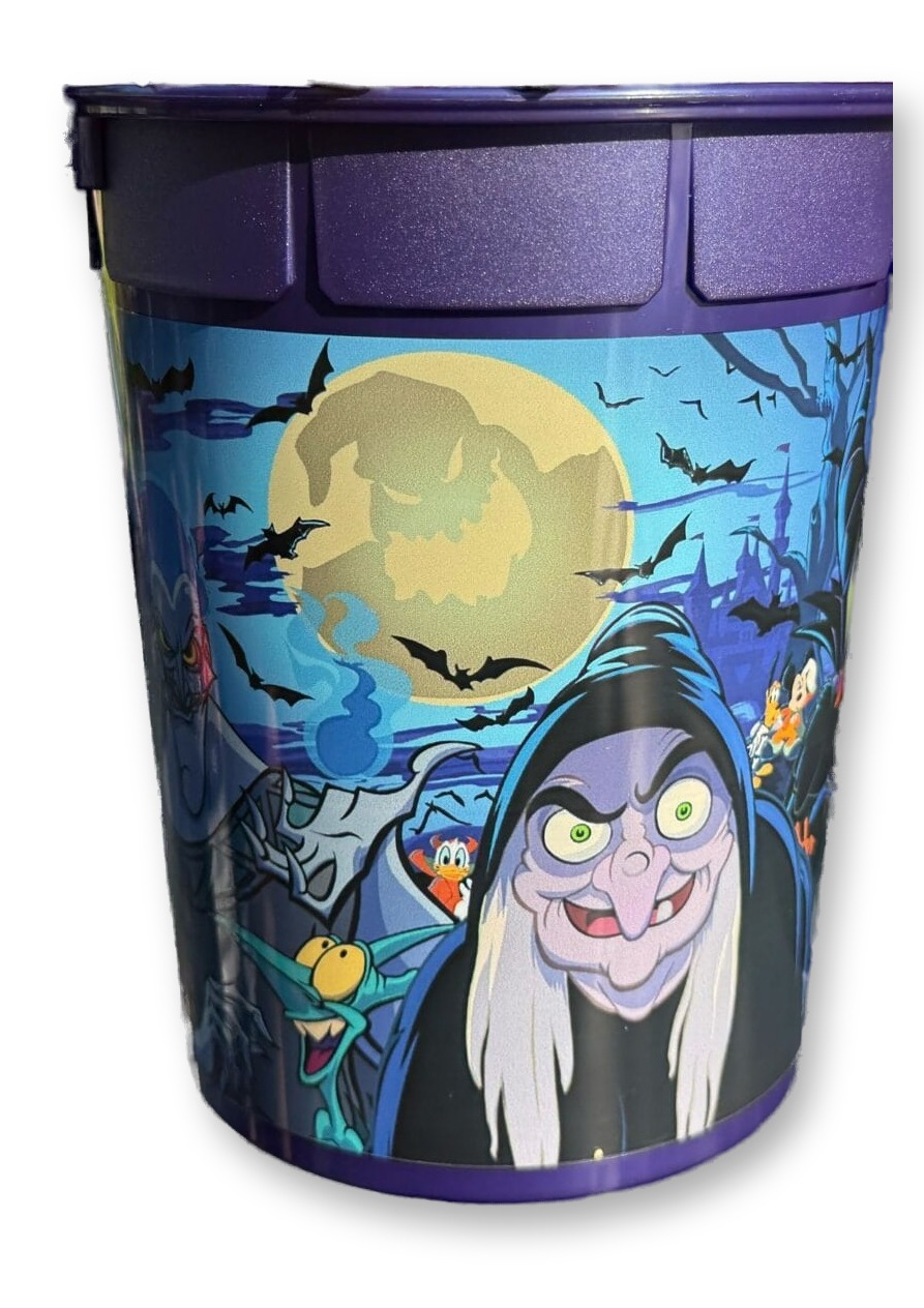 Hand holding a purple Disney Villains-themed popcorn bucket filled with popcorn, with a witch character illustration wrapped around the cup, outdoors at Disneyland