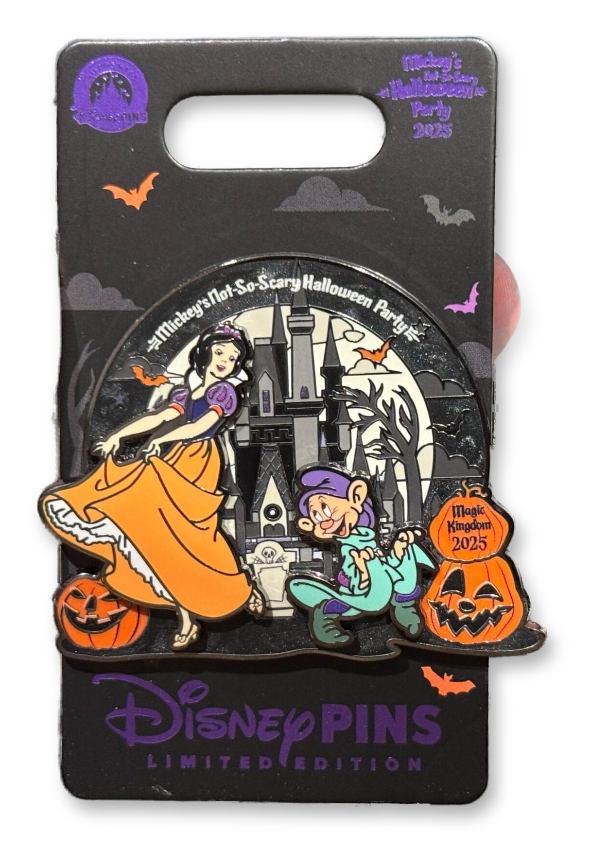 A hand holding an enamel Disney trading pin on its retail card, showing Snow White in an orange dress dancing next to Dopey in green, in front of a black-and-white Cinderella Castle with jack-o'-lanterns, bats, and 'Mickey's Not-So-Scary Halloween Party 2025' text.
