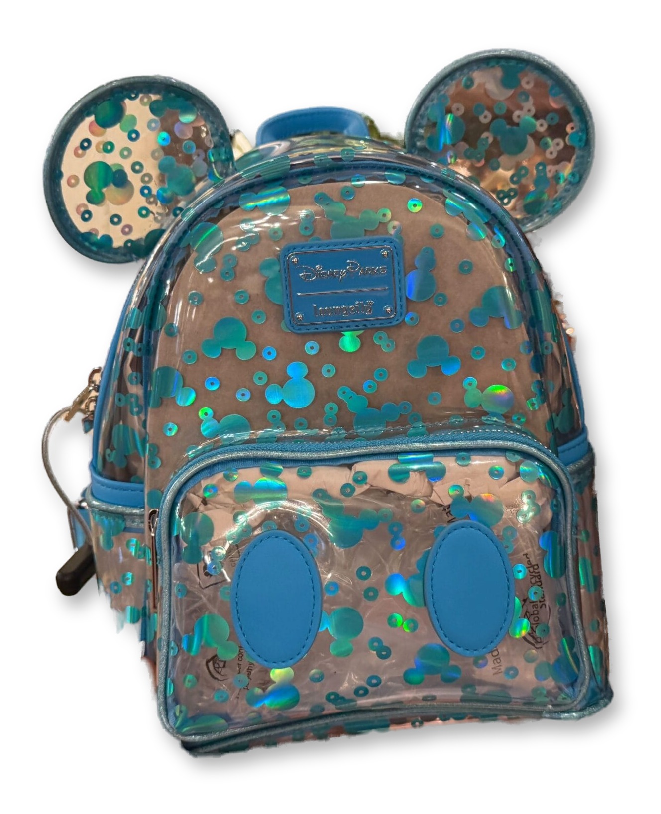 A hand holds up a clear plastic Loungefly mini backpack covered in holographic teal-blue sequins in a Mickey Mouse icon pattern, with clear sequined Mickey ears on top, in a Disney Parks merchandise shop with sparkly bags on shelves behind it.
