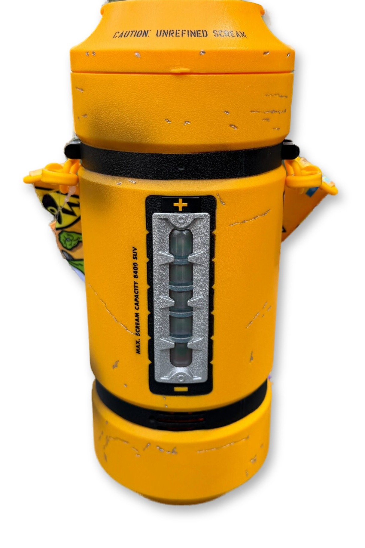 Yellow cylindrical popcorn bucket printed with 'Caution: Unrefined Scream' and a twist lock lid, shown standing on a wooden table with its illustrated Monsters, Inc. character strap draped beside it.