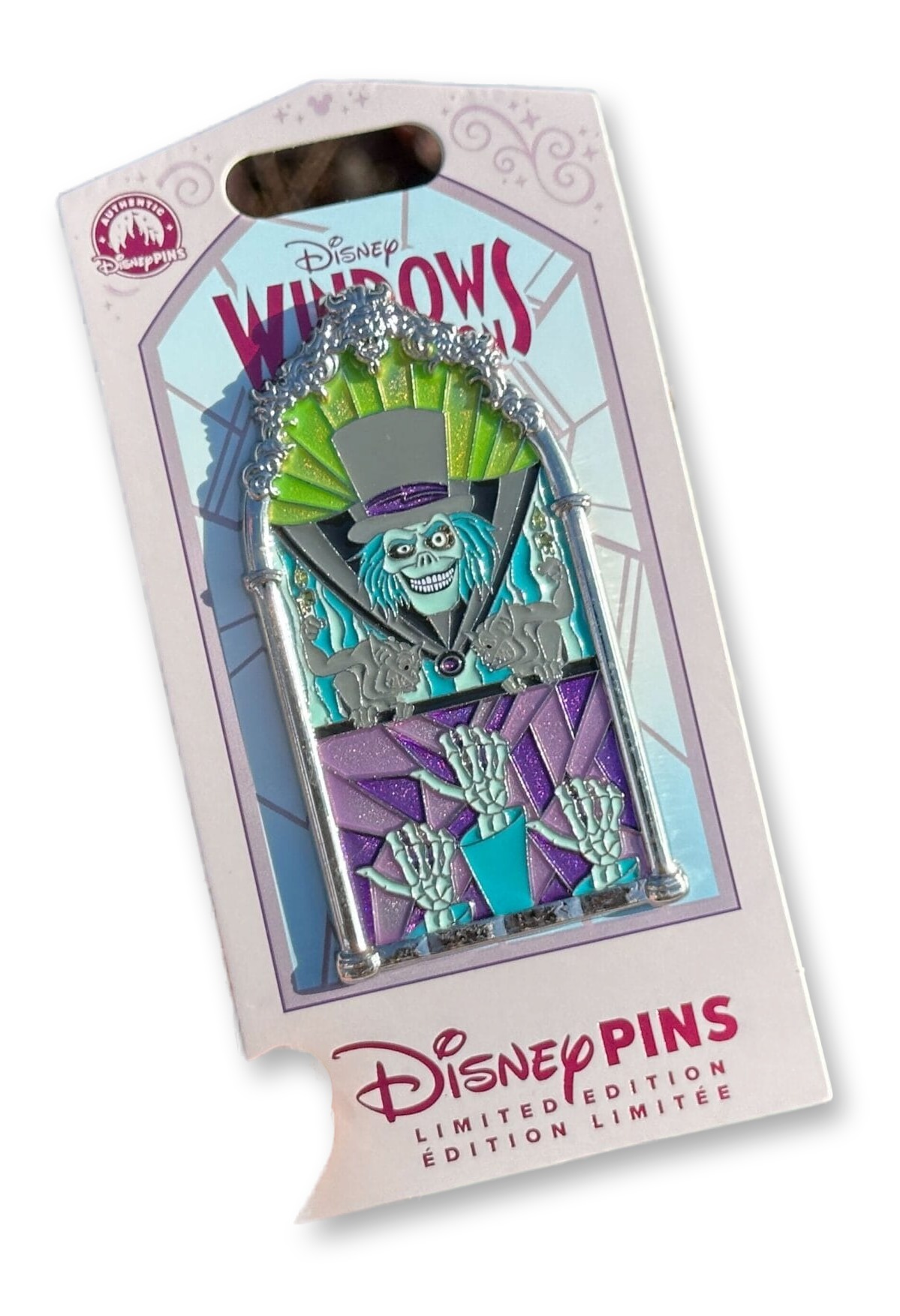 Stained-glass lancet window-shaped pin featuring the Haunted Mansion's Hatbox Ghost between two gargoyles above three skeletal hitchhiking-ghost hands.