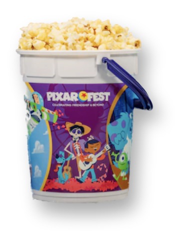 White plastic Pixar Fest 2024 popcorn bucket with a purple wraparound band illustrated with Coco, Monsters Inc., and Turning Red characters, filled with popcorn, next to its navy lid