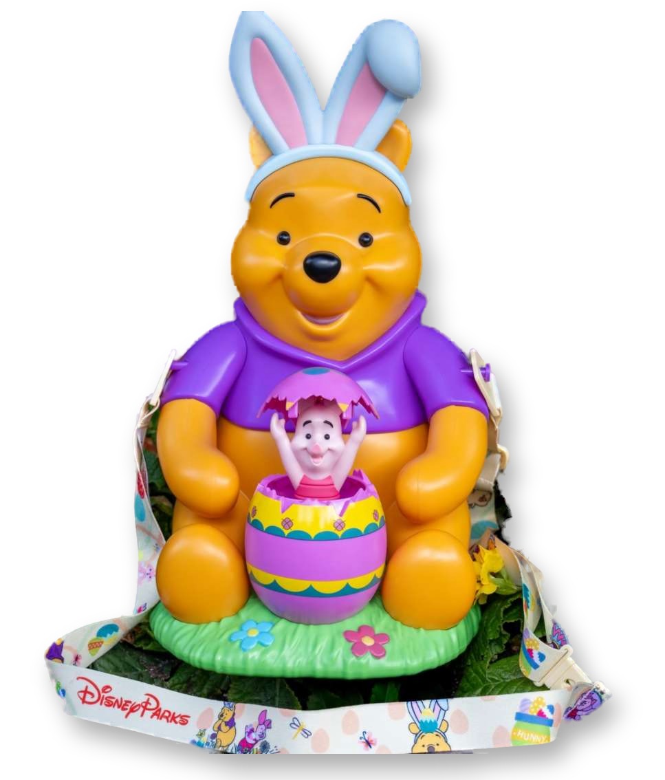 White and purple figural popcorn bucket of Winnie the Pooh wearing bunny ears, with Piglet popping out of an Easter egg in front of him, set among garden flowers